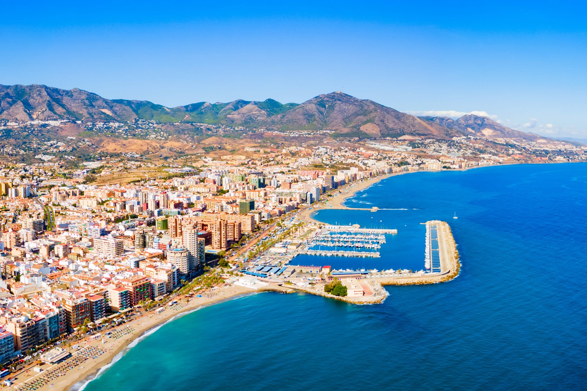 Fuengirola from the air: the marina, the long town beach and the apartment blocks along the front, with the Sierra de Mijas behind