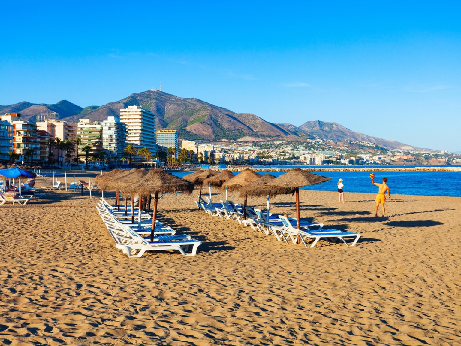 Straw umbrellas and sun loungers on Fuengirola beach, with the apartment blocks of the front and the Sierra de Mijas behind