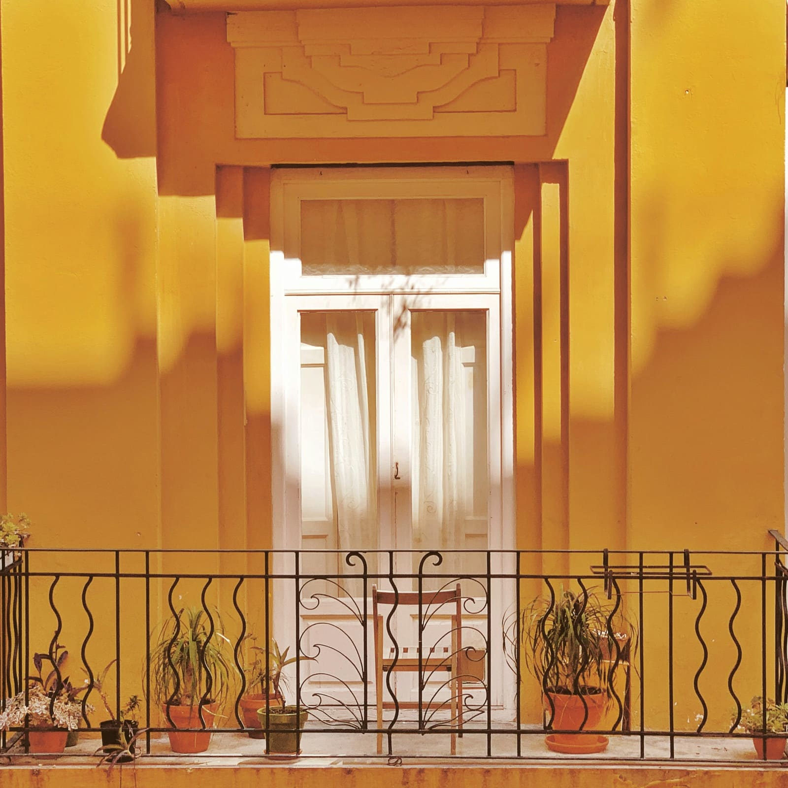 A balcony with potted plants in front of a white door, on a yellow house front
