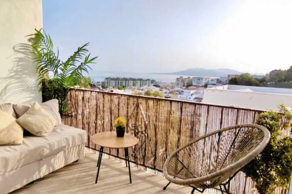 A terrace with a sofa and a sea view over a white town at dusk