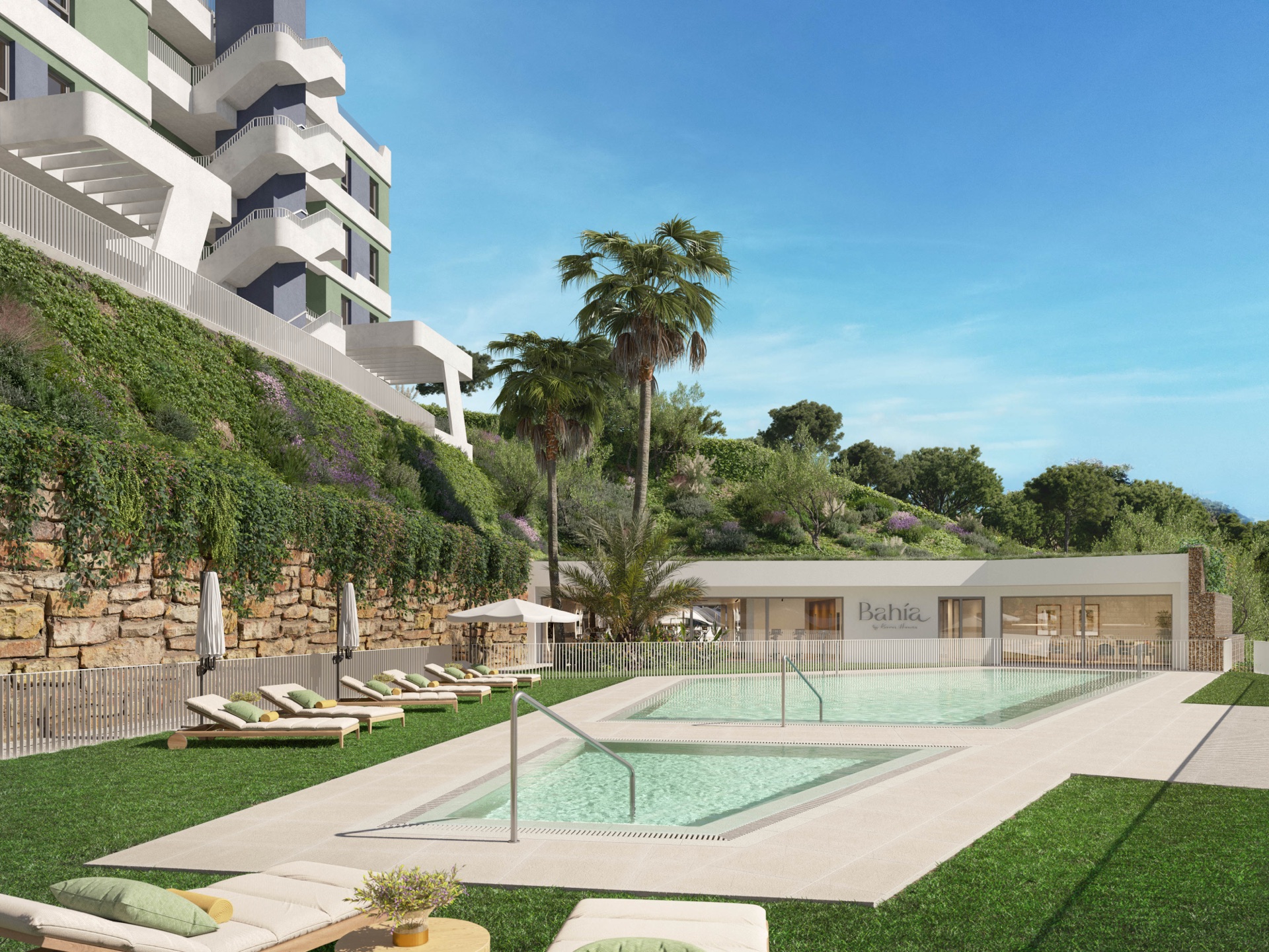 The pool by day, with sun loungers on a lawn below the buildings. Bahía, La Cala de Mijas, Mijas.