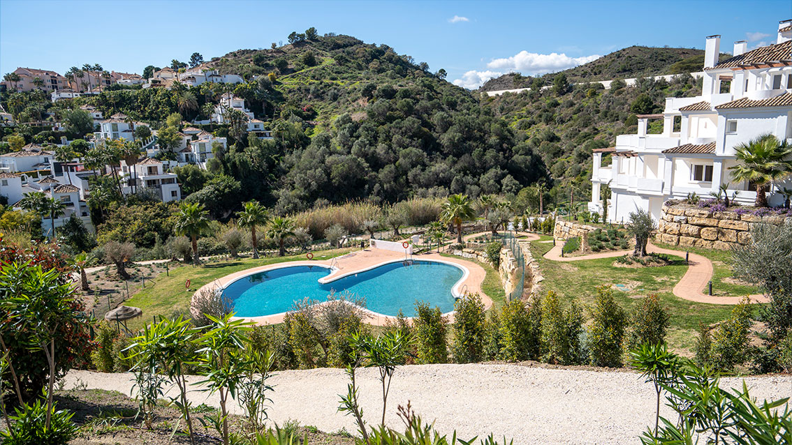 A pool set in the gardens, with planted paths and wooded hills behind. Be Aloha, Nueva Andalucía, Marbella.