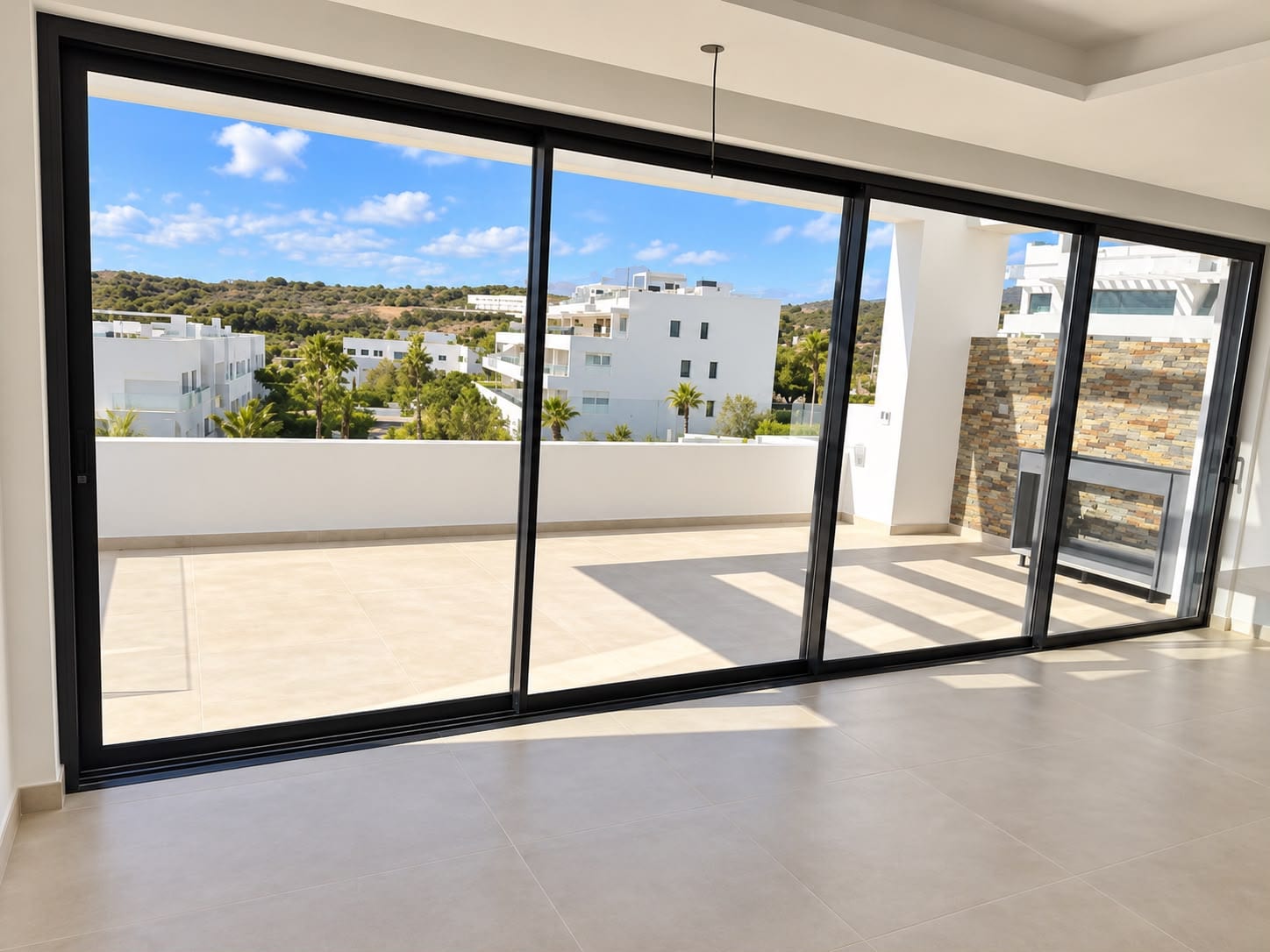 The living room of a finished home, with a wall of sliding glass doors onto the terrace and its outdoor kitchen. Costafiore Gardens, Arroyo Enmedio, Estepona.