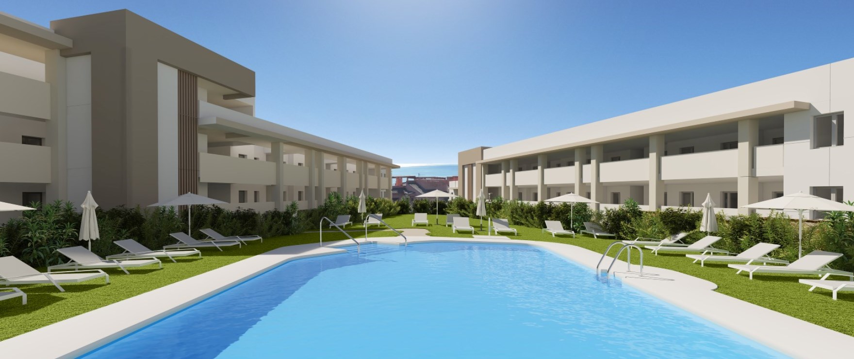 A pool between two of the buildings, with loungers set out on the lawn along one side. Grand Bay, Bahía de las Rocas, Manilva.