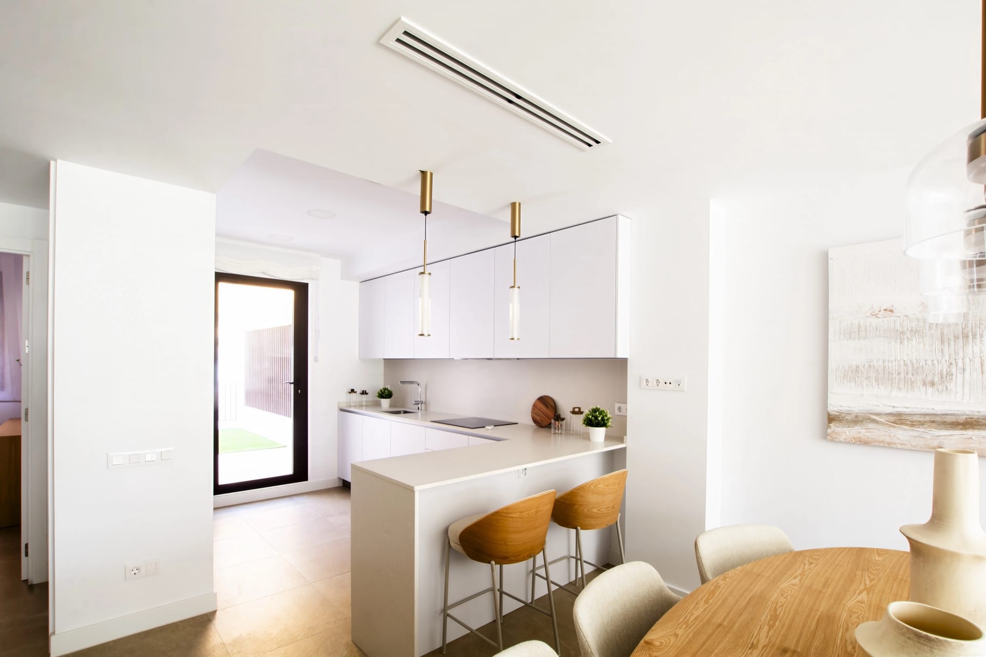 The kitchen, with white units, a breakfast bar and a glass door to the garden. Idilia Meraki, Torre de Benagalbón, Rincón de la Victoria.