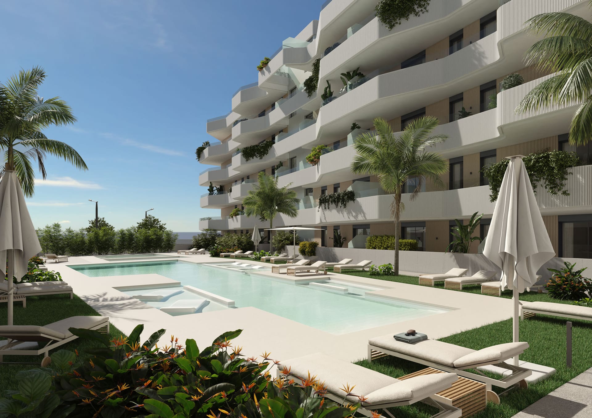The main outdoor pool, with loungers on the lawn beside it and one of the buildings behind, its balconies hung with plants. Laguna Suites, Las Lagunas de Mijas, Mijas.