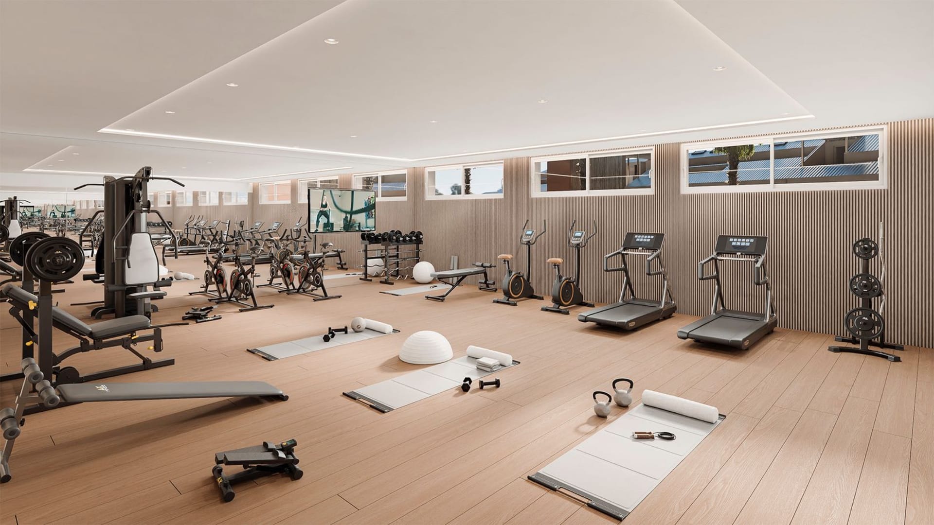 The gym, with machines and free weights on a timber floor under a row of high windows. Lomas Unique, El Higuerón, Fuengirola.