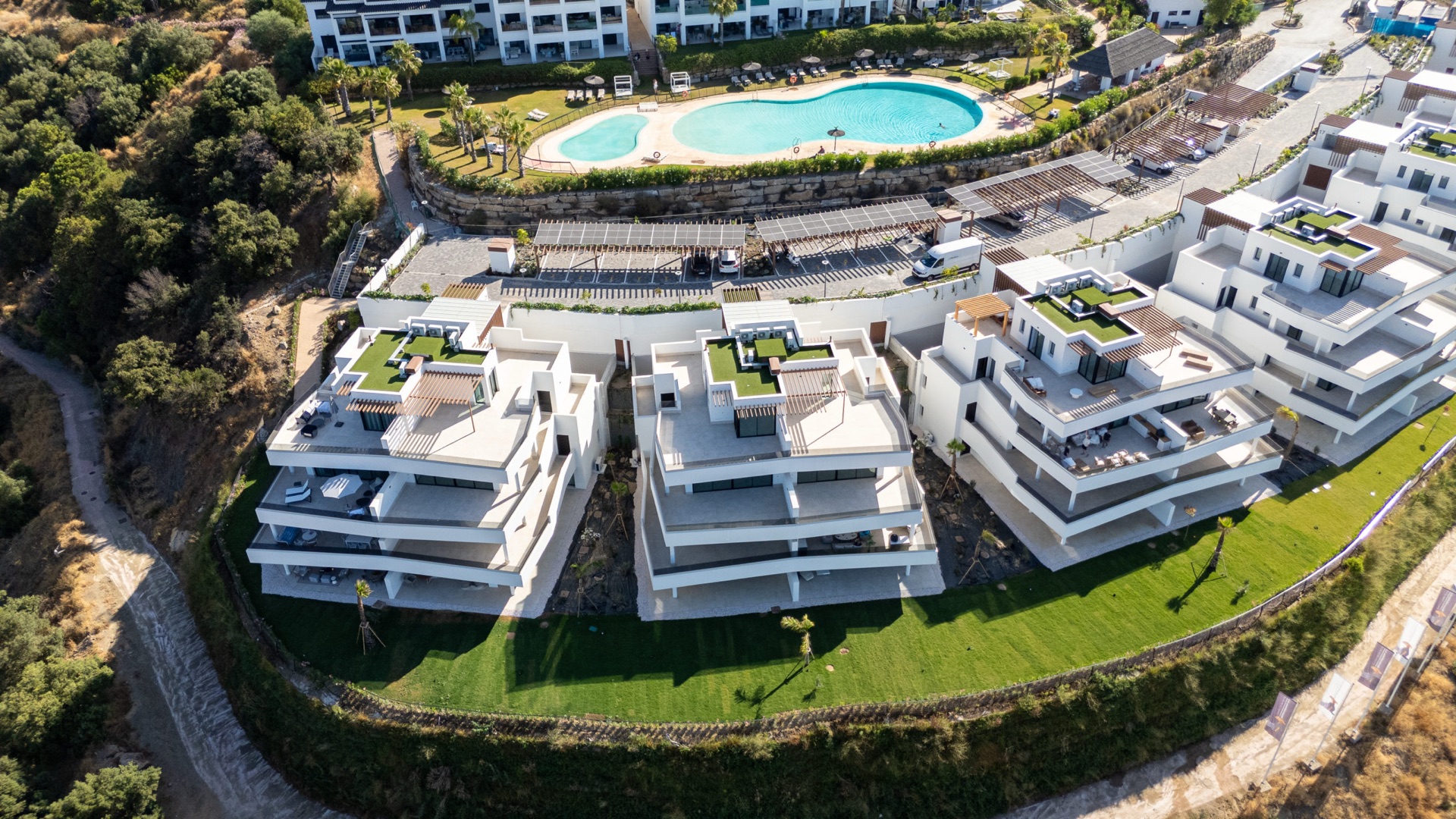 The finished first stage of Vista Hermosa from above, with a lawn in front of the buildings, parking under solar panels behind them and one of the resort’s pools on the level above. Mirador de Estepona Hills, Altos de Estepona, Estepona.