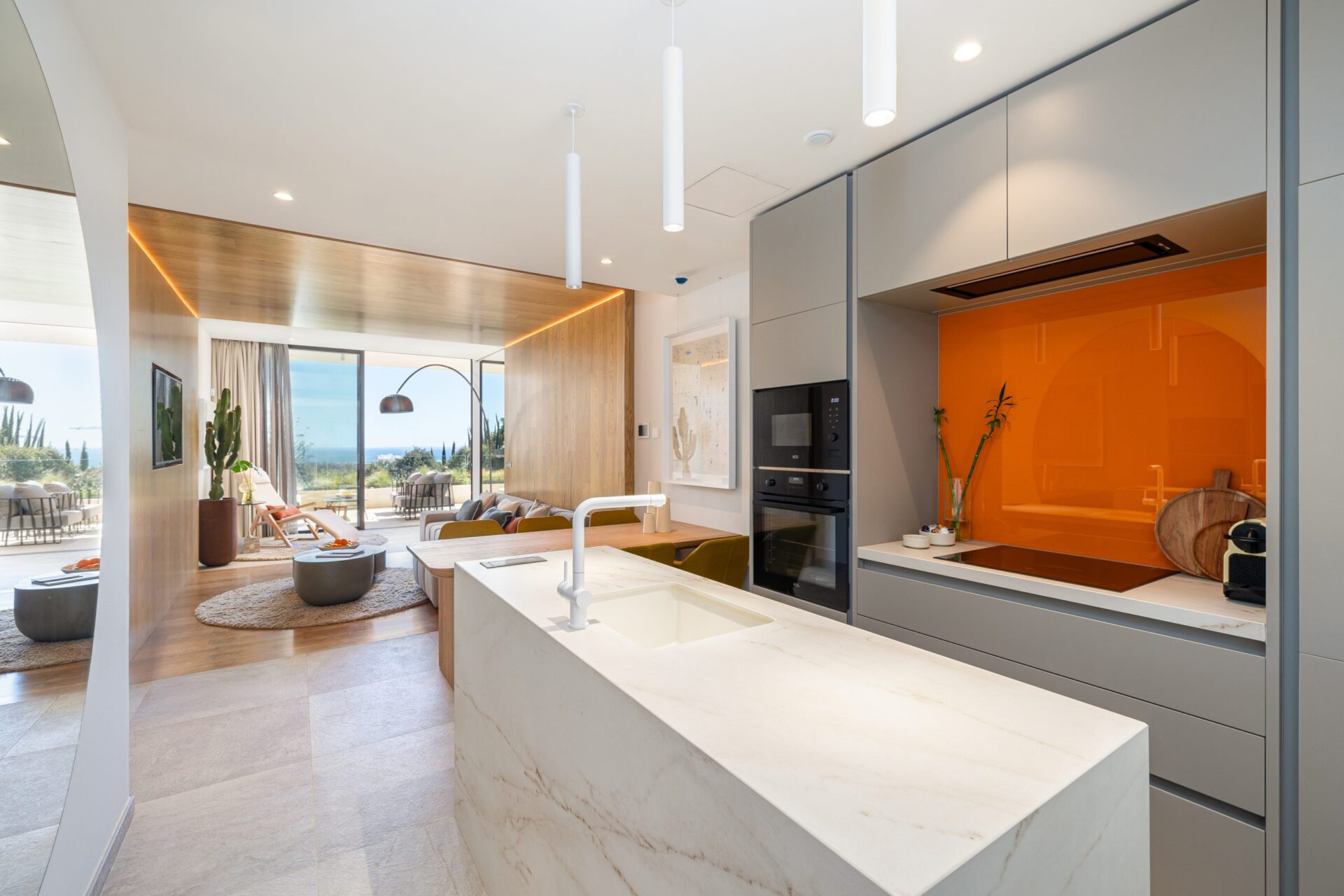The kitchen, with a white stone island and an orange glass wall behind the hob. North Residences, El Higuerón, Fuengirola.