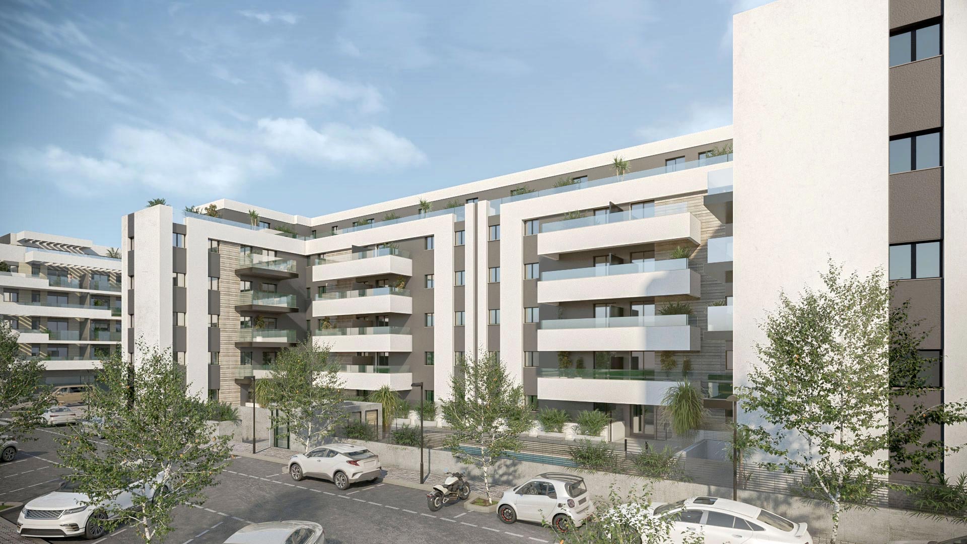 The corner of the buildings from the street, with trees along the pavement. Premier Residencial, Las Lagunas, Mijas.