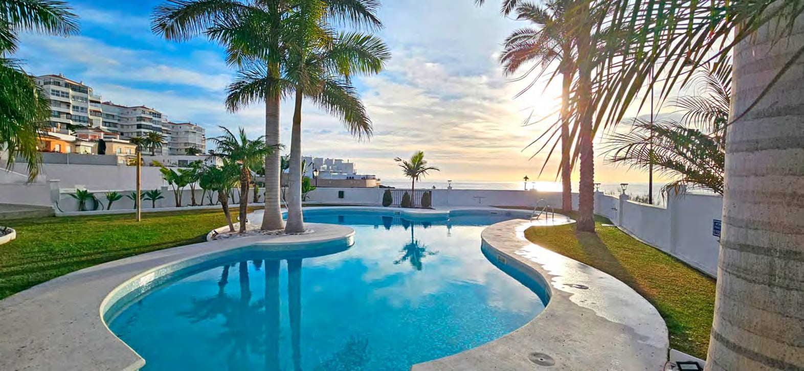 The communal pool, set in lawns under palm trees, with the sea on the horizon. Residencial Peñoncillo, El Peñoncillo, Torrox.