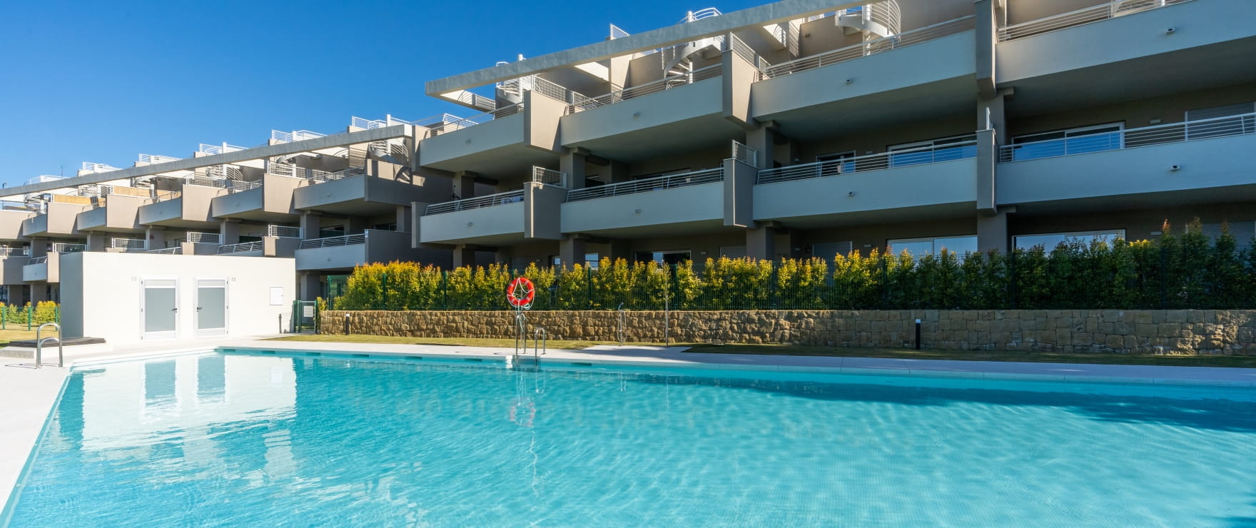 The pool, with the stepped terraces of the apartments rising behind a hedge and a low stone wall. Sunny Golf, Estepona Golf, Estepona.