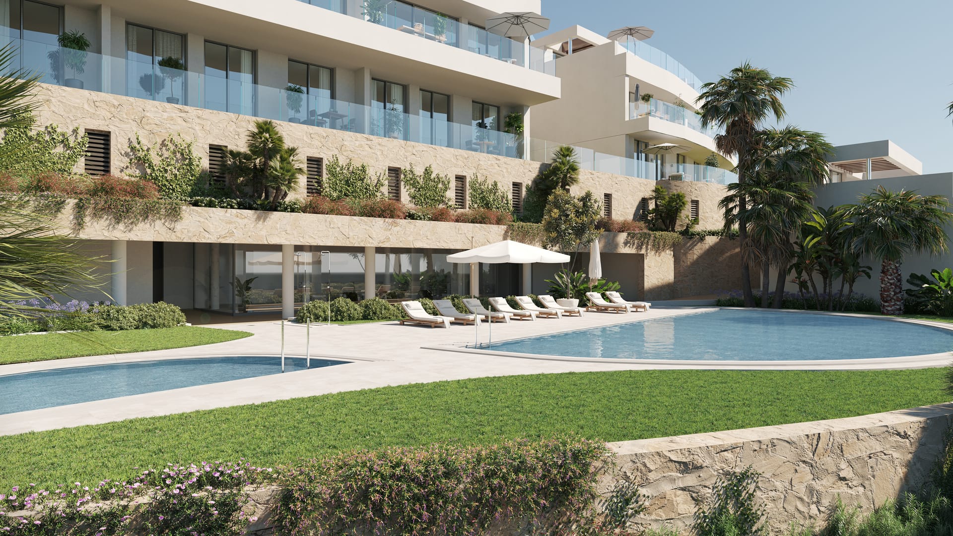 The shared pools at the foot of the new development, with sun loungers on the lawn beside them. The Kos, El Higuerón, Fuengirola.