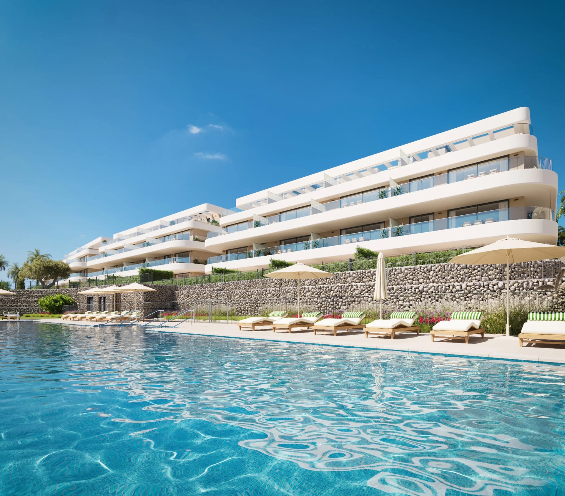 The outdoor pool, with loungers and parasols along a stone wall below the buildings. Unika Collection, Buenas Noches, Estepona.