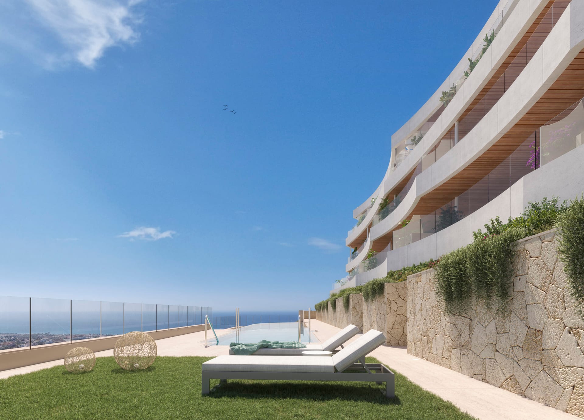 The shared pool along the foot of the building, with a lawn, sun loungers and a glass rail looking out to sea. Victoria Hills, Torre de Benagalbón, Rincón de la Victoria.
