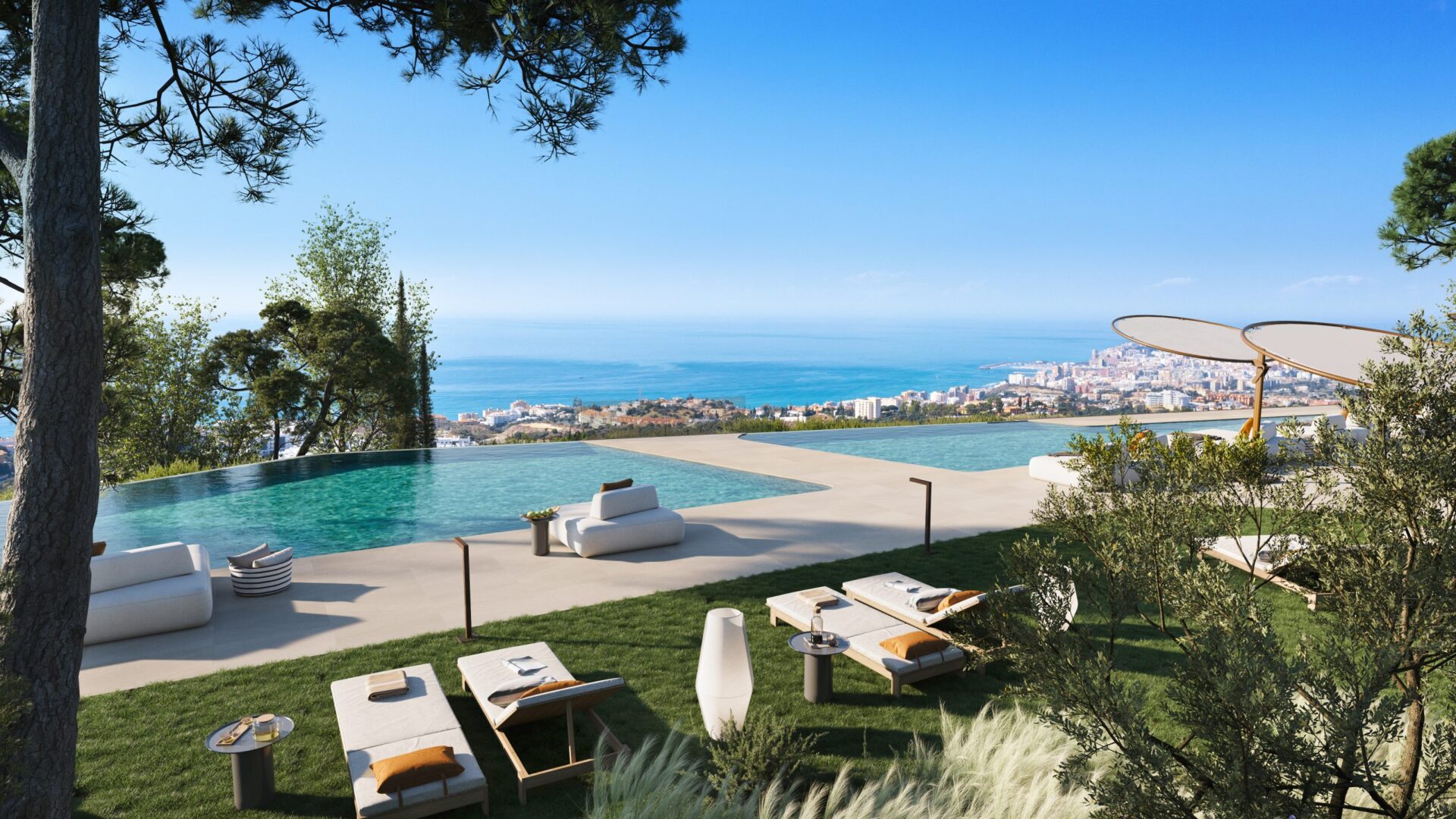 An infinity pool set into a lawn, with sun loungers and the coast in the distance. Waterfall Residences, El Higuerón, Fuengirola.