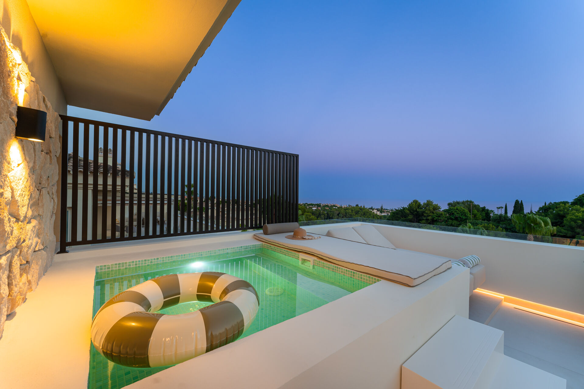 The heated plunge pool on the terrace at dusk, with a daybed beside it and a slatted screen behind.