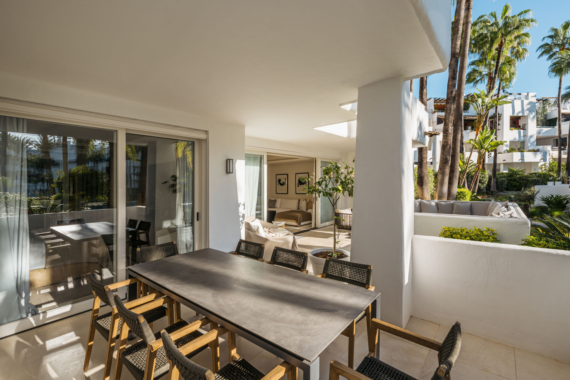 The dining table on the covered terrace, with glass doors into the apartment on the left and a built-in sofa among the plants on the right.