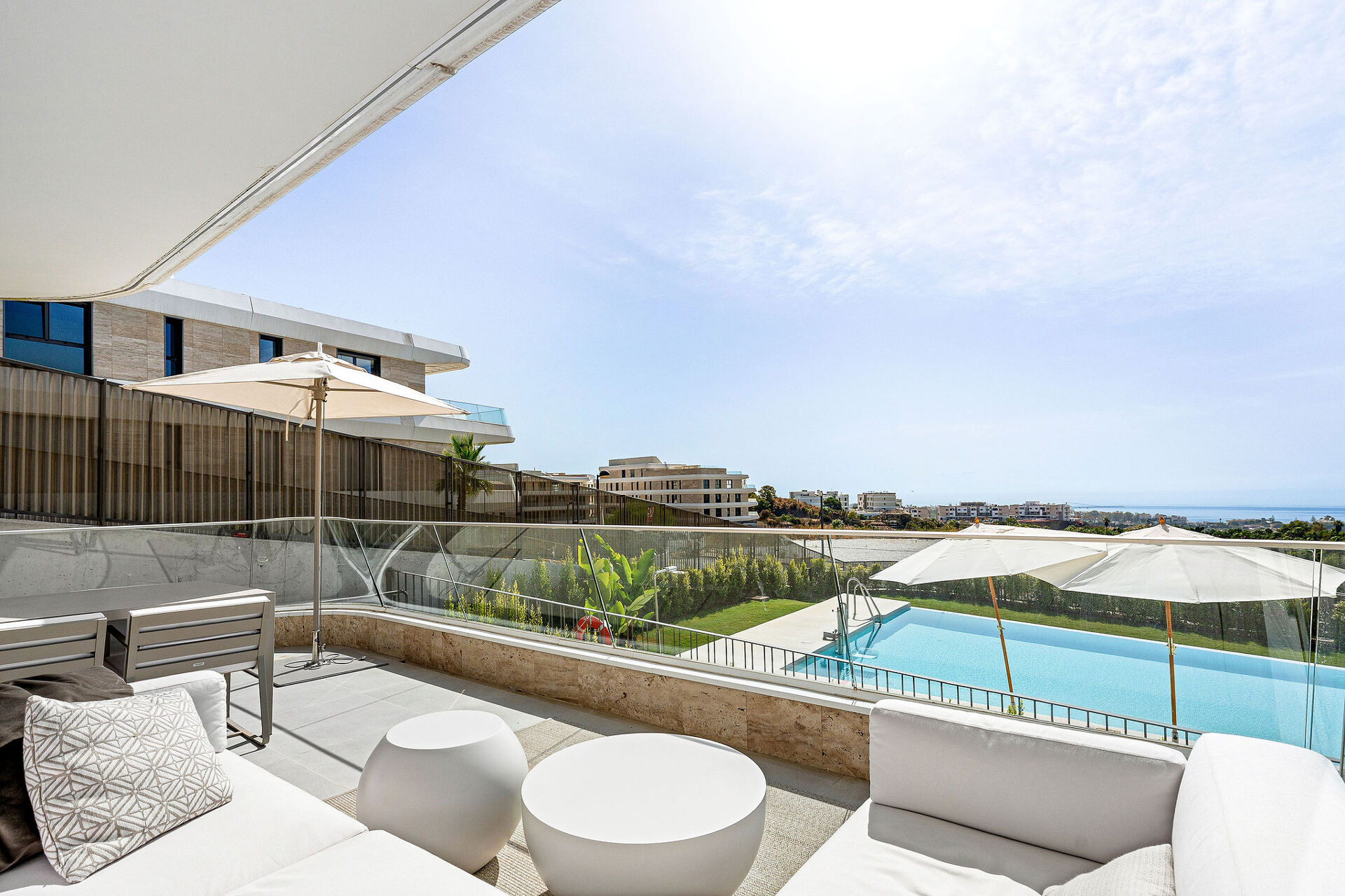 The terrace, with outdoor sofas and a dining table, above the communal pool and with the sea on the horizon.