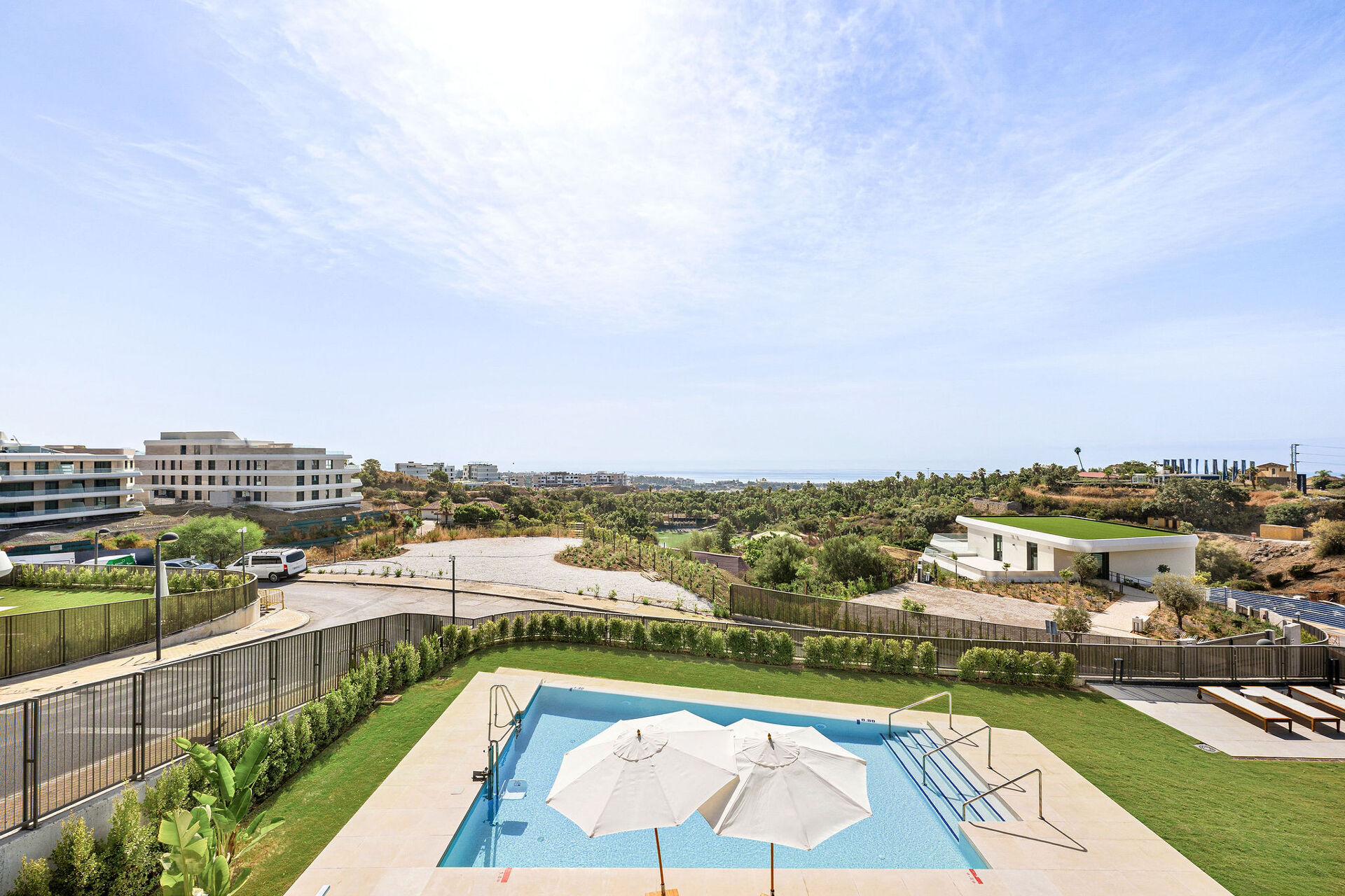 The communal pool with its lawn and parasols, and the hillside and the sea in the distance.