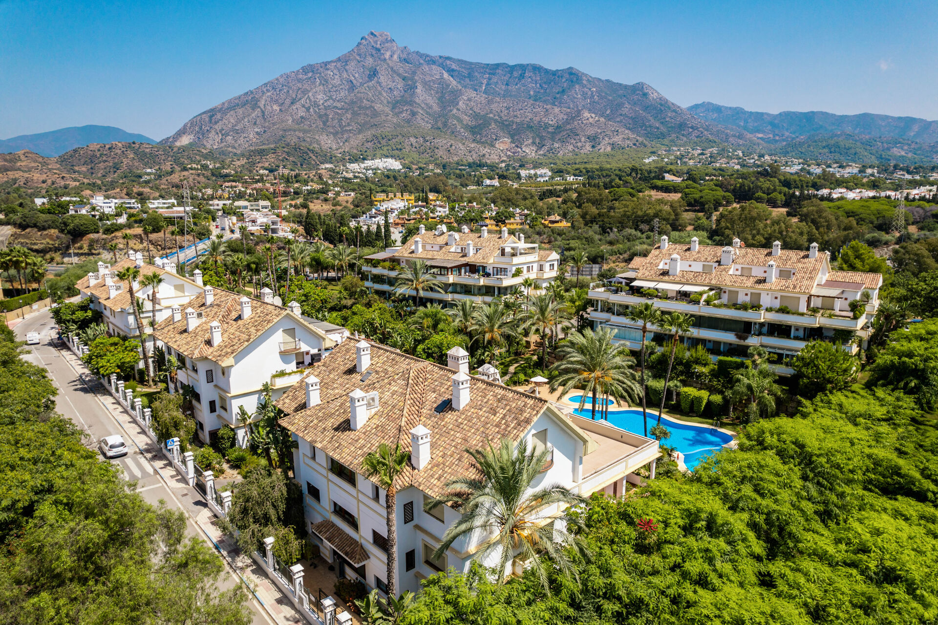 An aerial view of tiled-roof apartment buildings, gardens and a swimming pool, with La Concha mountain behind.