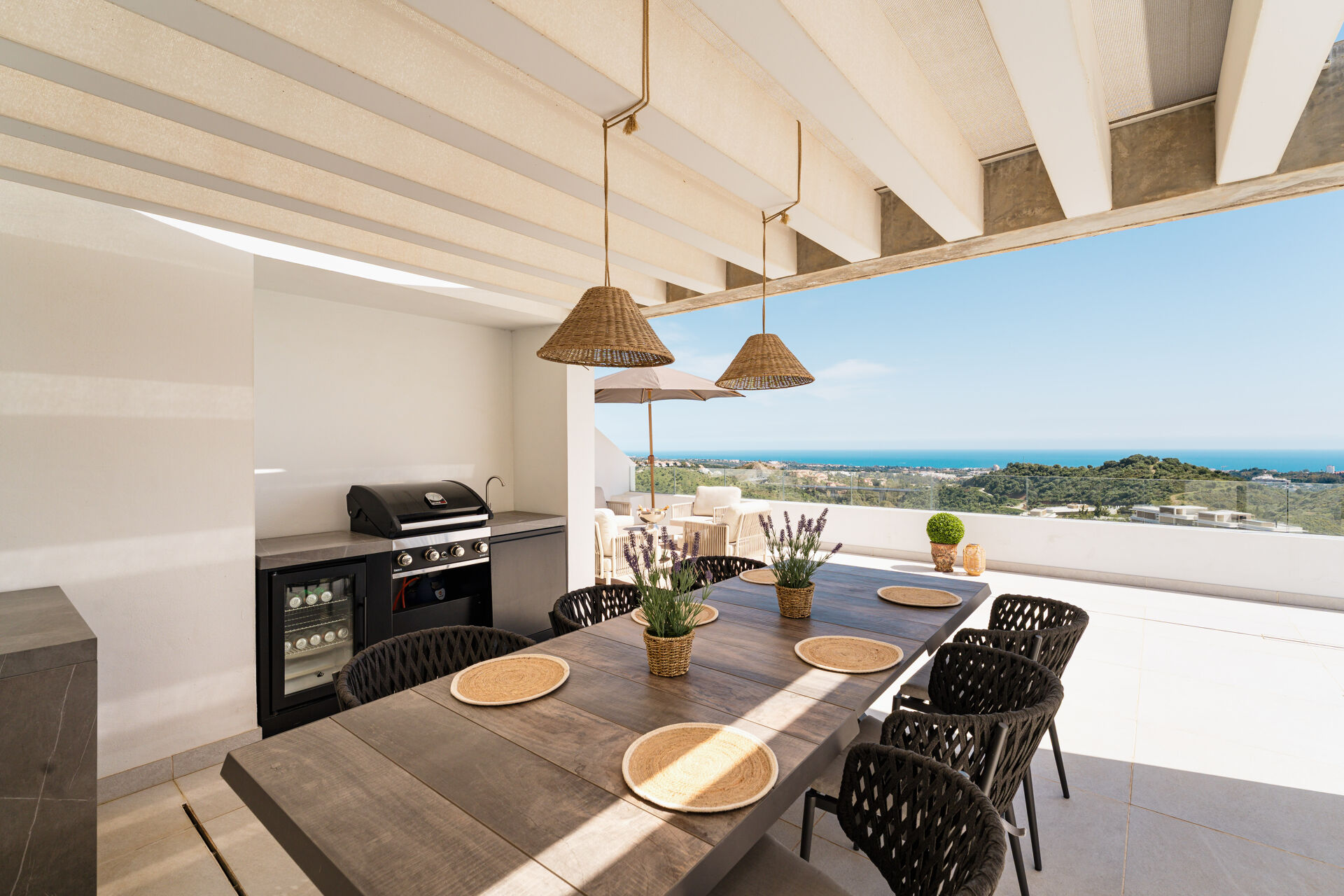 The outdoor kitchen on the solarium, with a barbecue, a wine fridge and a long dining table under a pergola, and the sea beyond.