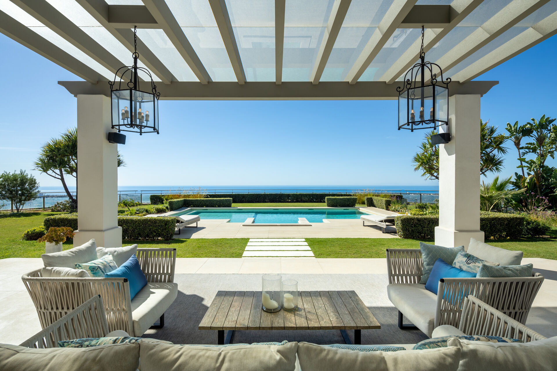 The covered terrace with outdoor seating, looking across the lawn to the swimming pool and the sea.