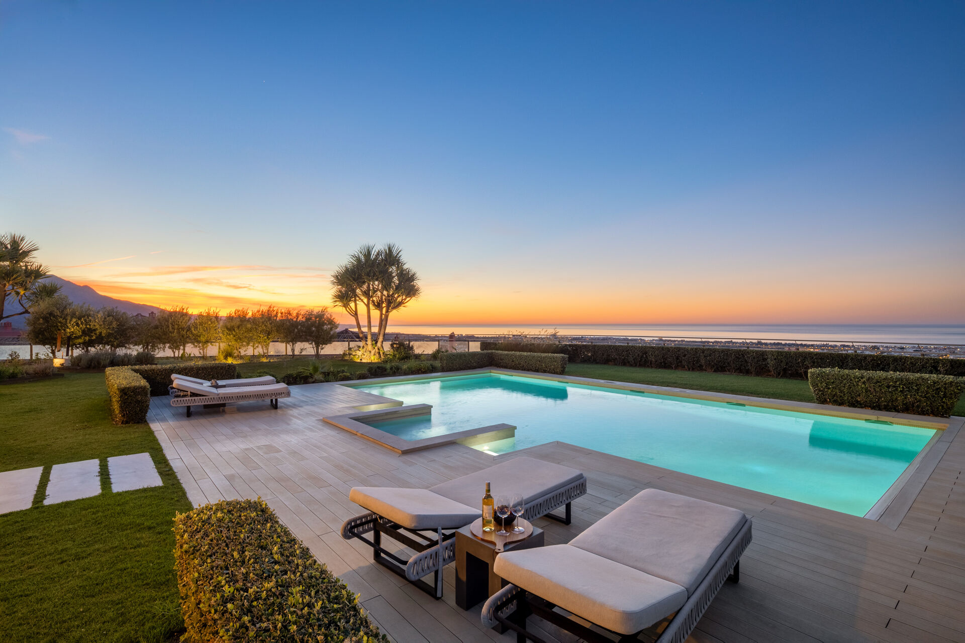 The swimming pool and sun loungers on the garden terrace at dusk, with the sea on the horizon.
