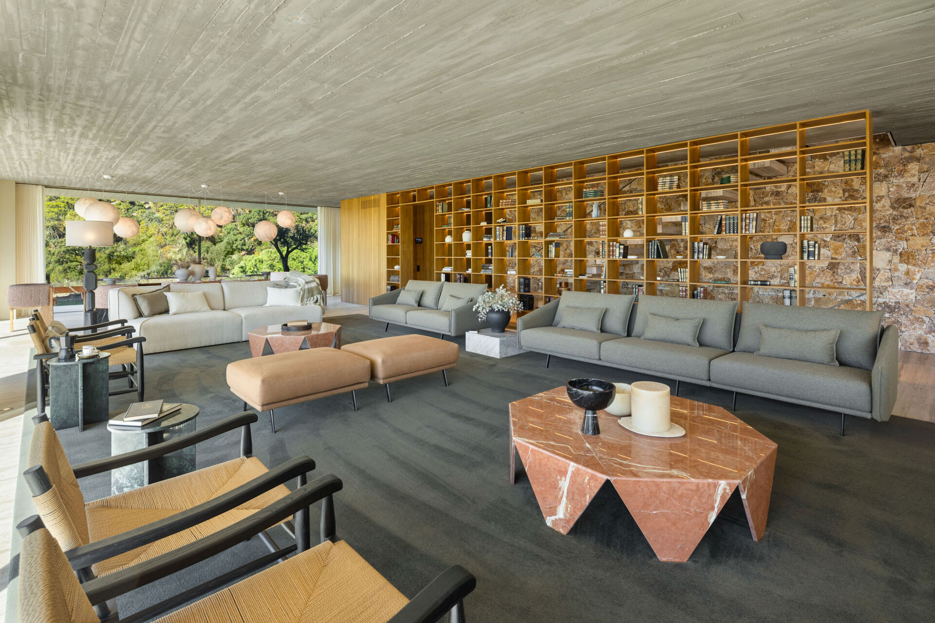 The living room, with grey sofas and a pink marble table in front of a long wall of lit timber shelving.