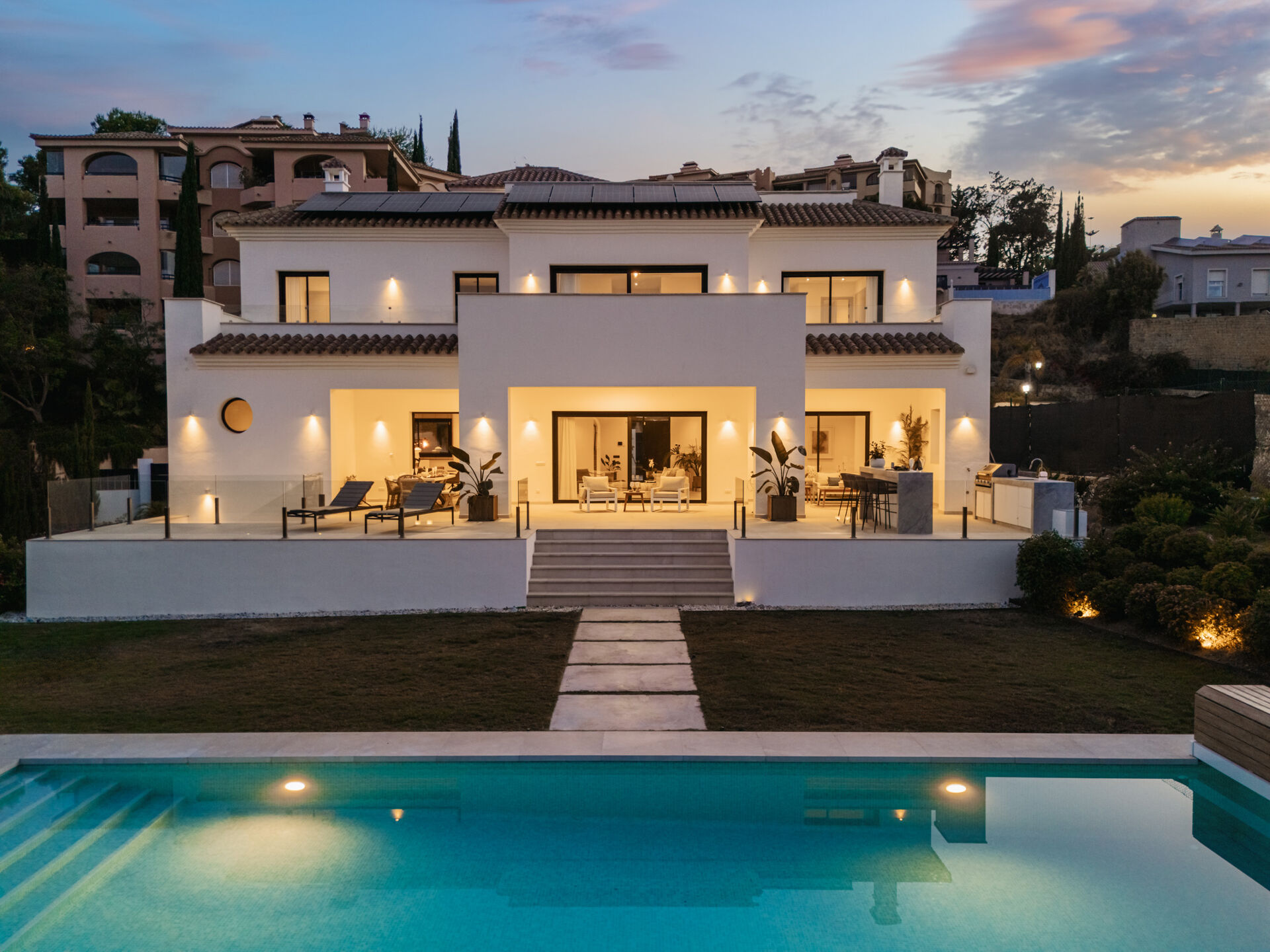 The back of the villa at dusk, with the lawn and the swimming pool in front.