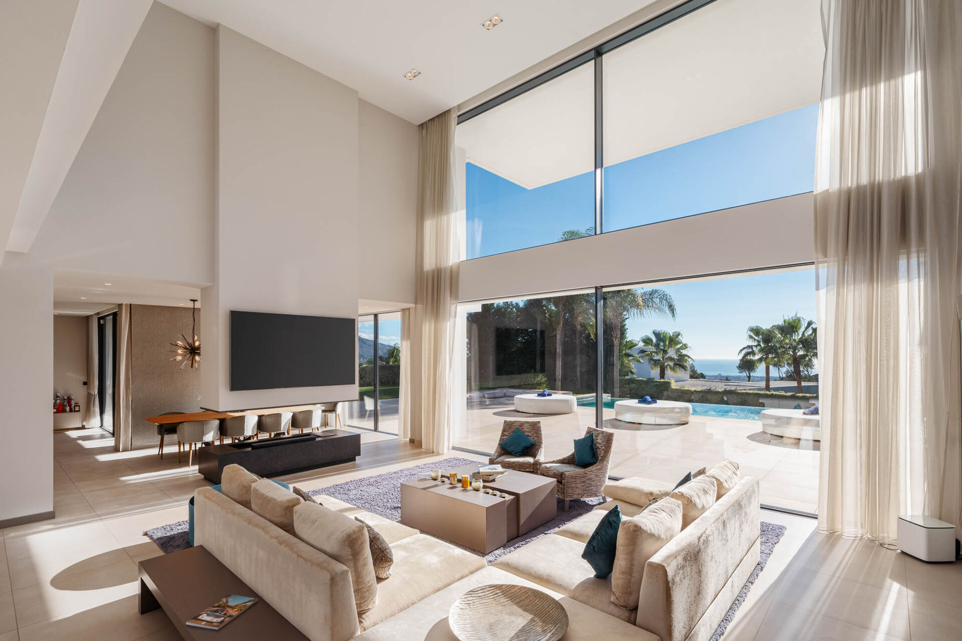 The double-height living room, with a corner sofa, armchairs and a large window onto the pool terrace and the sea.