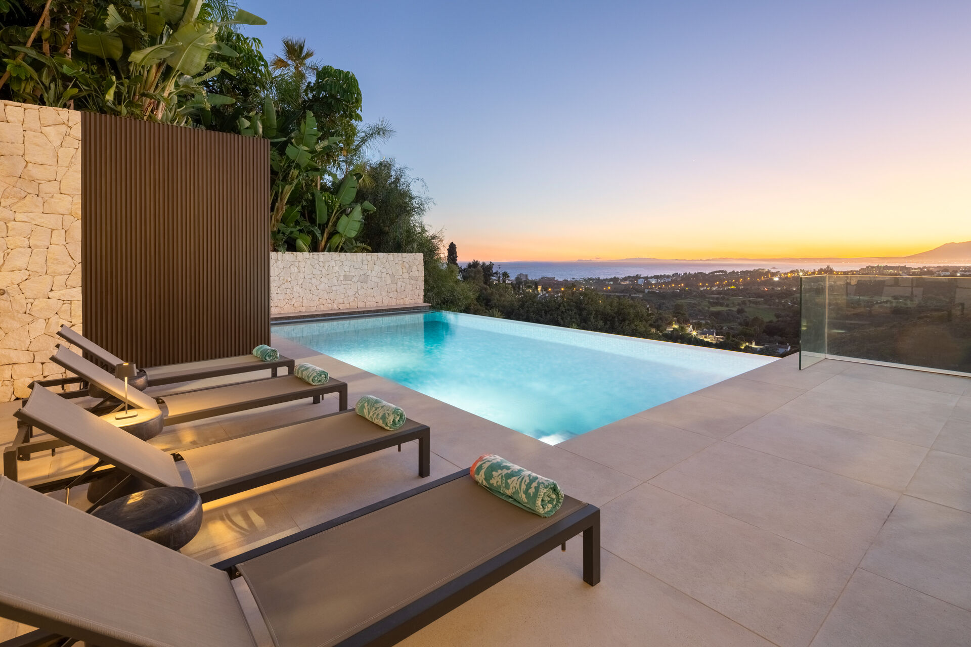 The swimming pool and sun loungers at dusk, with the sea and the coast in the distance.