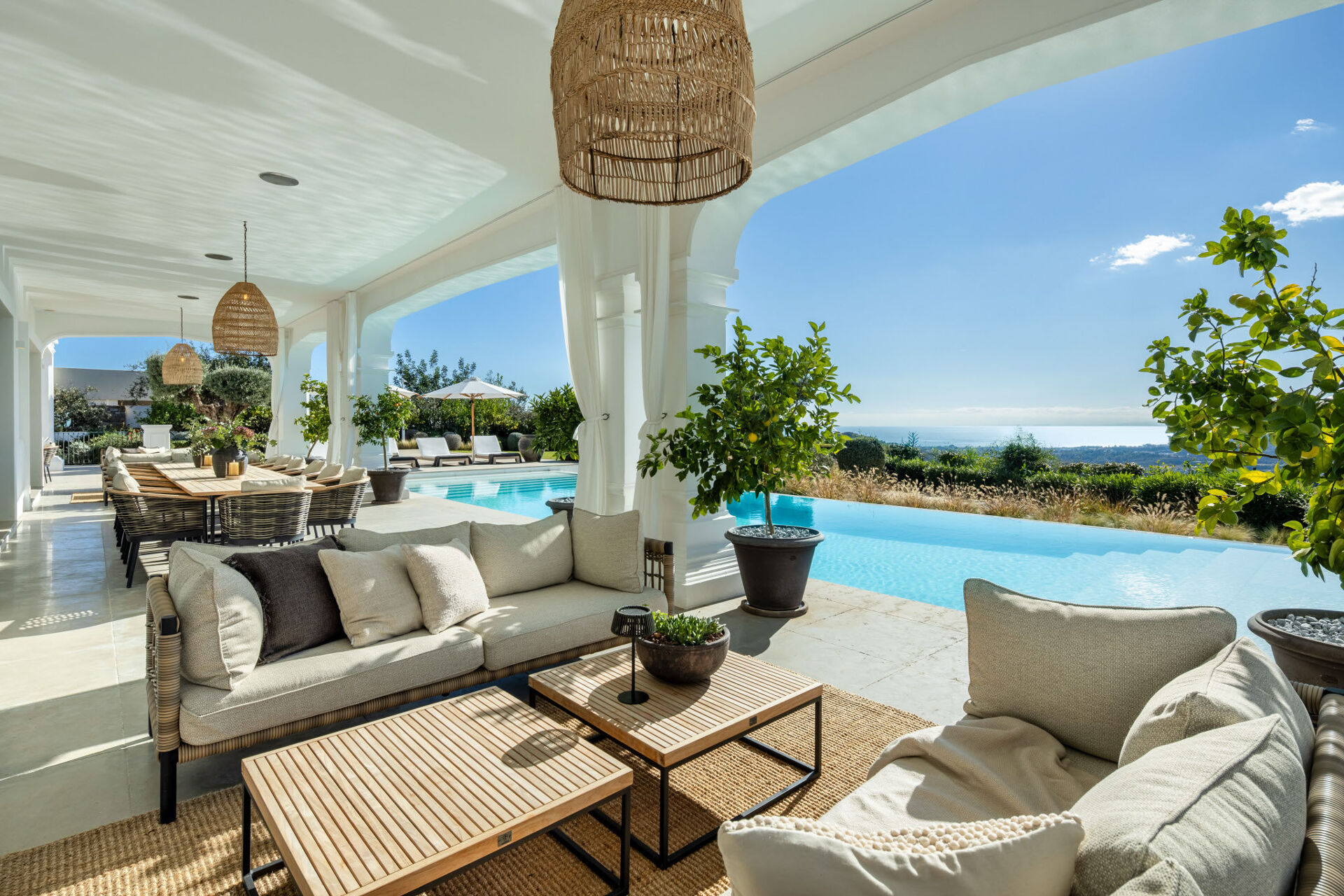 The covered terrace with sofas and a dining table beside the infinity pool, looking out towards the sea.
