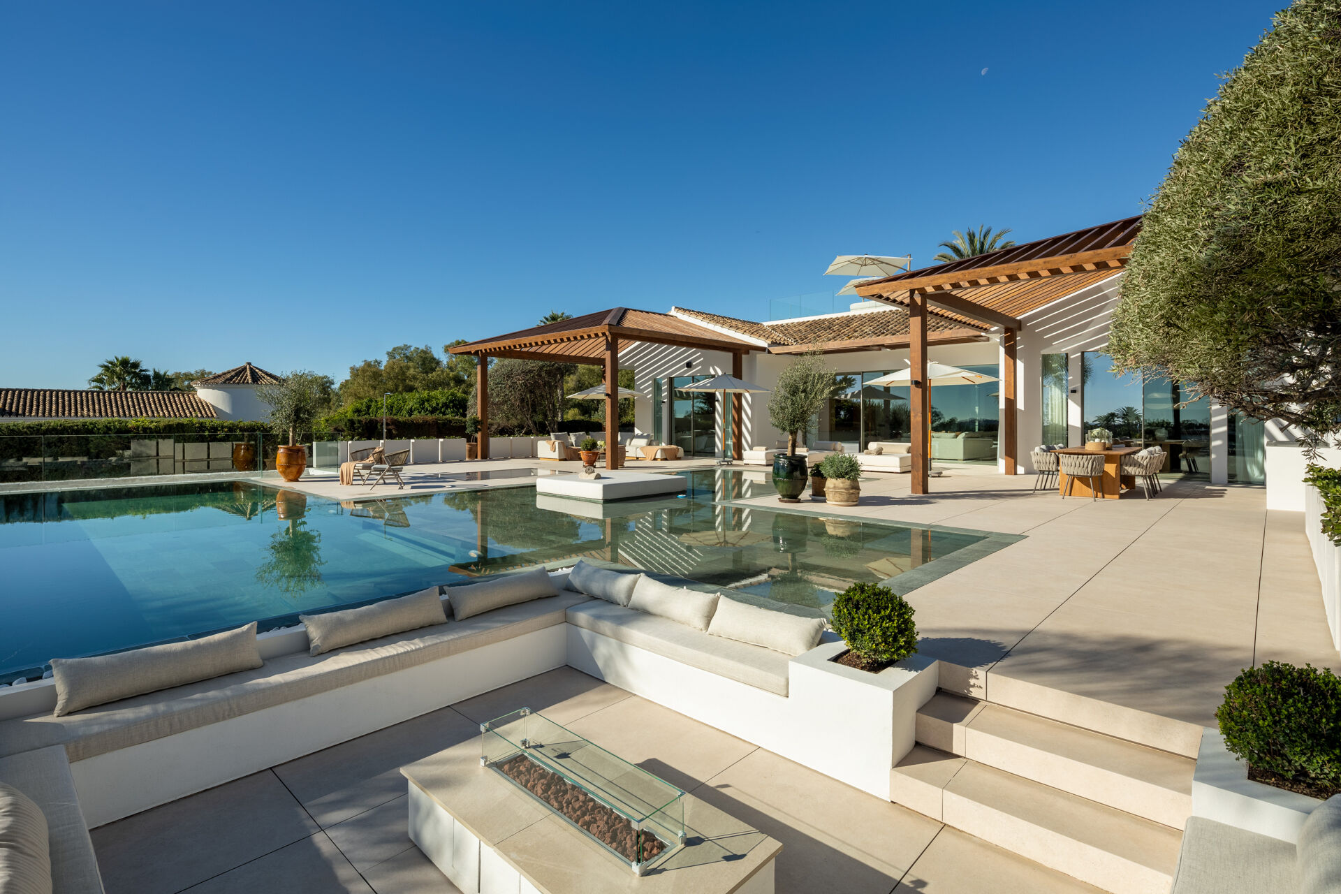 The swimming pool, a sunken seating area with a fire table and the covered terraces beside the villa.