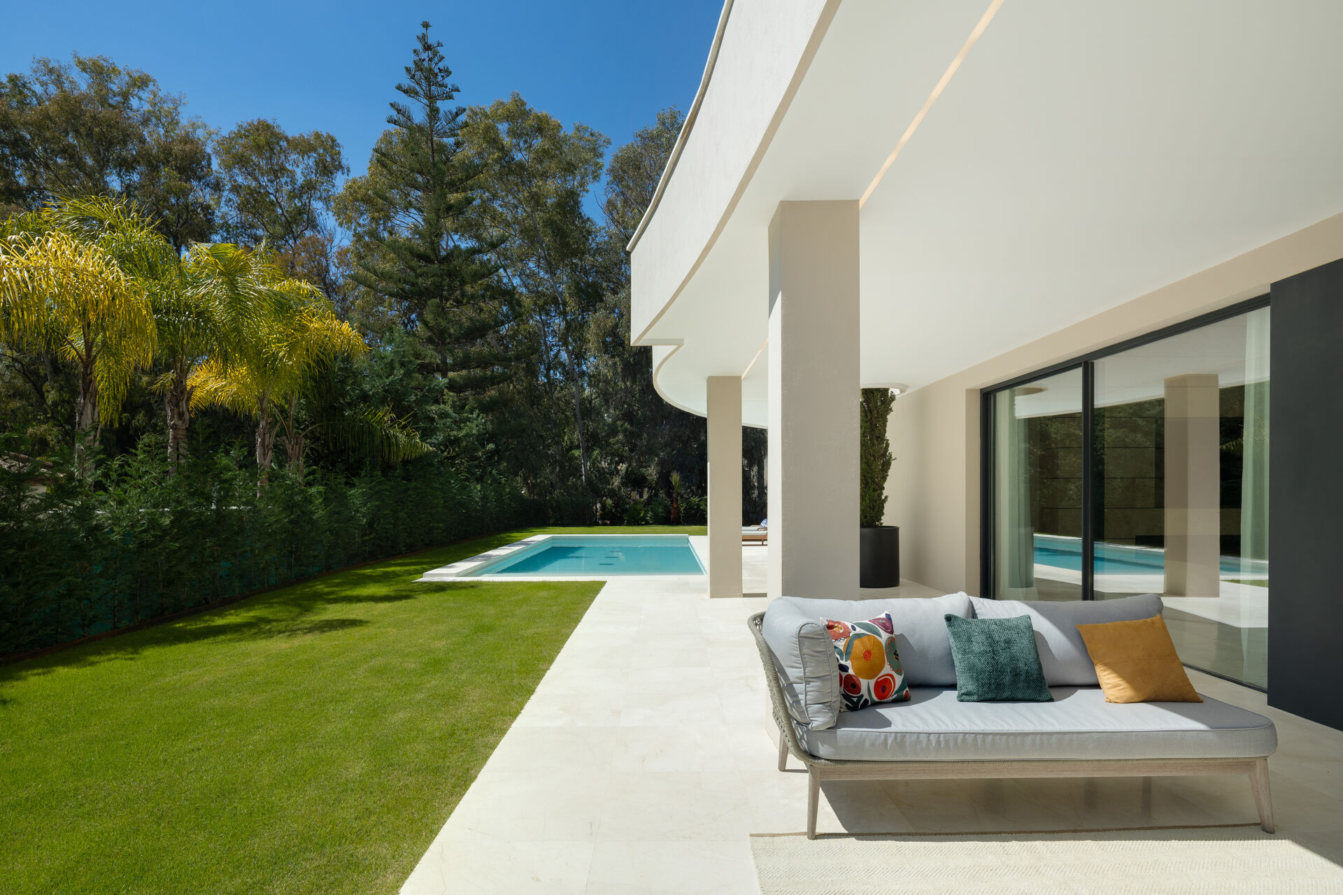 The lawn and the covered terrace on the garden side of the villa, with the swimming pool beyond.