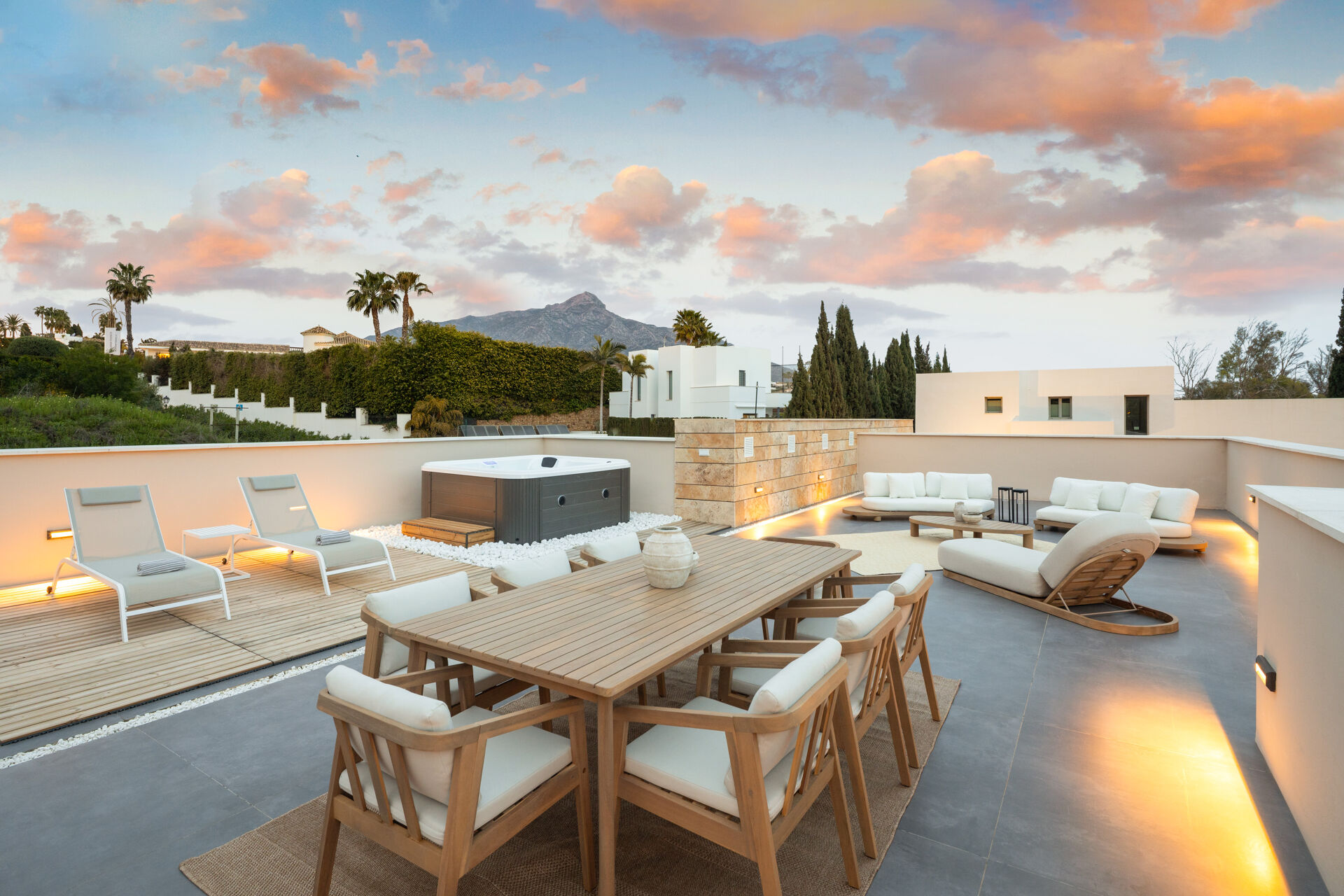 The roof terrace with a dining table, lounge seating and a hot tub, with a mountain in the distance.