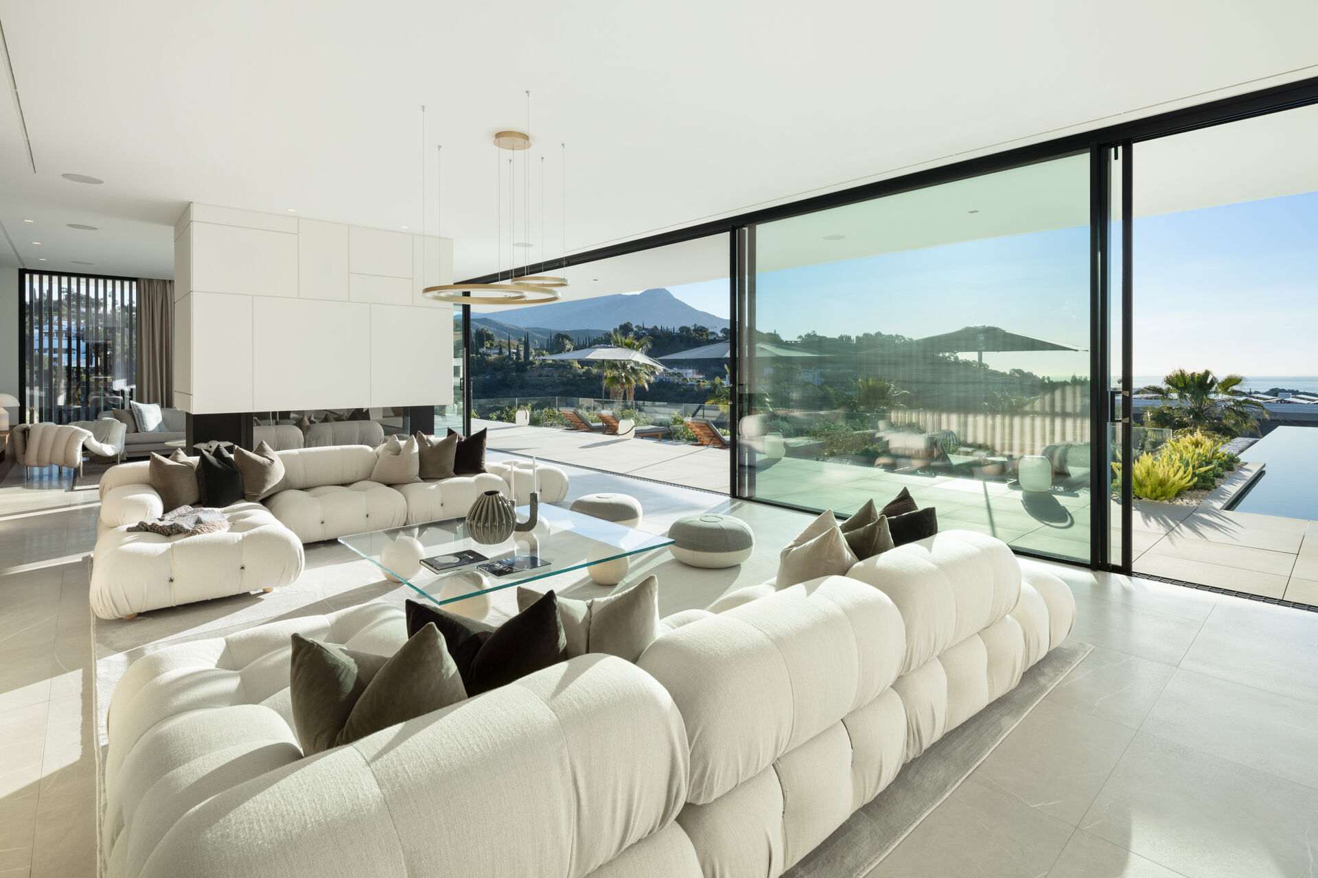 The living room, with white sofas around a glass table and sliding glass walls open to the terrace and the pool.