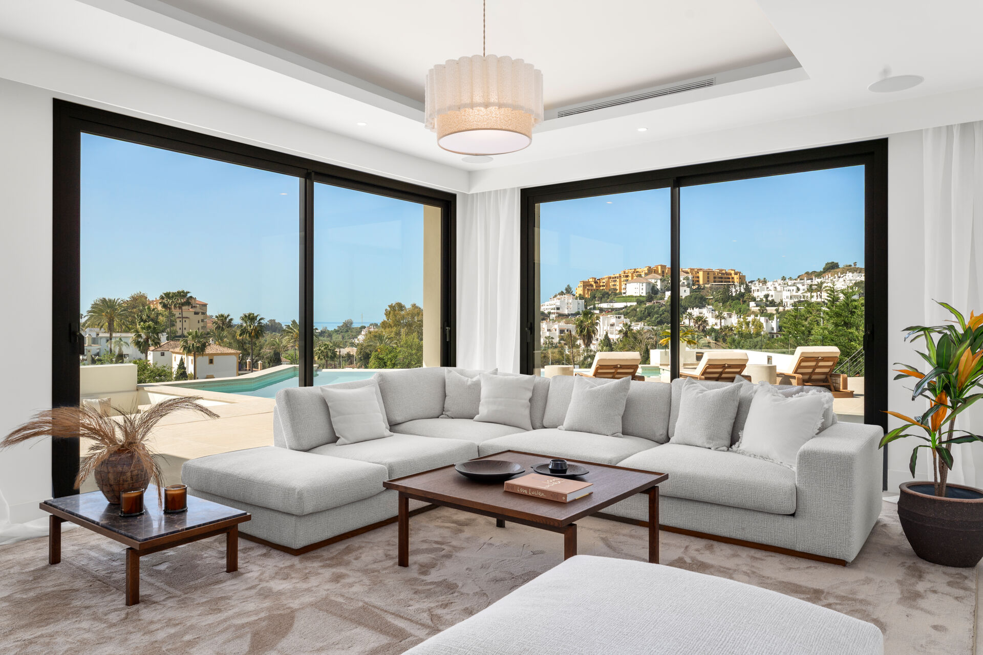 The living room, with a large corner sofa and floor-to-ceiling glass doors facing the terrace and the pool.