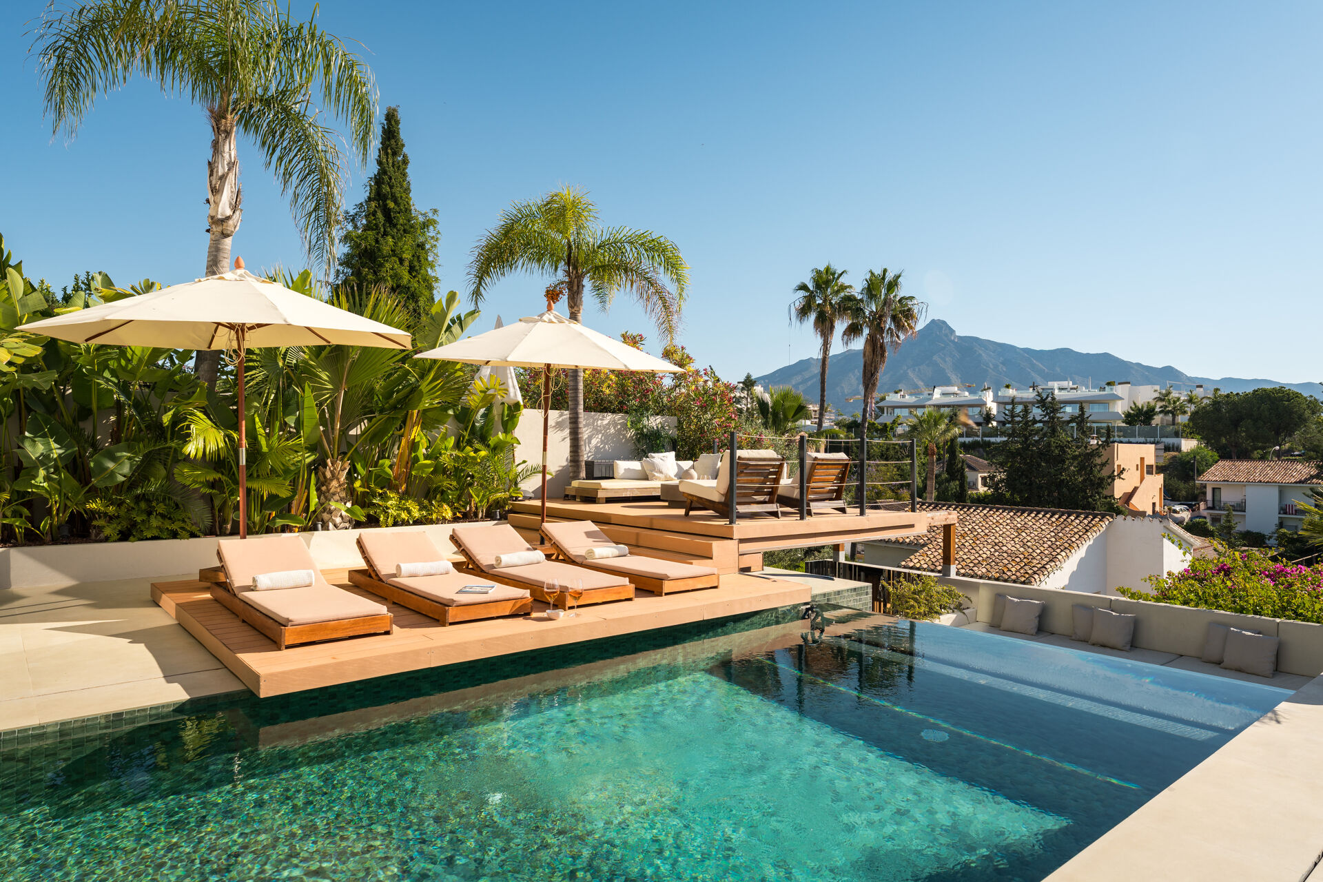 The swimming pool with sun loungers on a timber deck and parasols, with La Concha mountain behind the neighbouring houses.