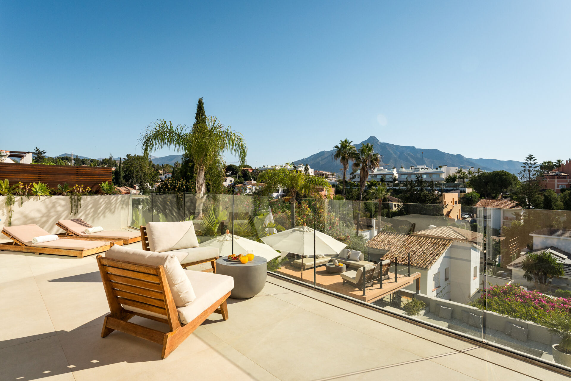 The upper terrace with sun loungers and armchairs behind a glass balustrade, looking over rooftops and gardens to La Concha mountain.